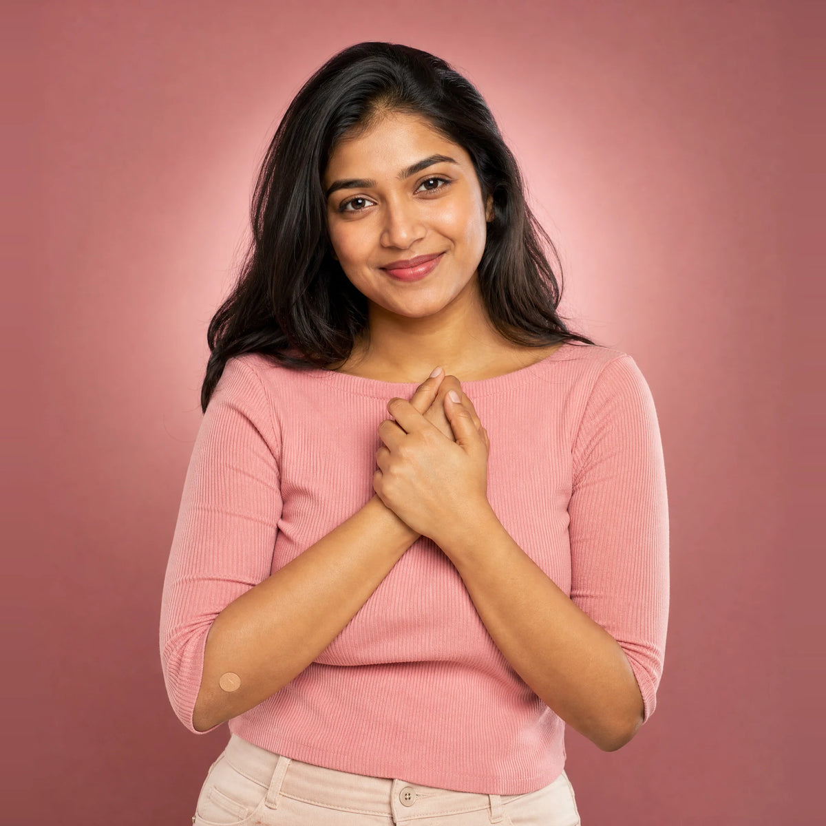 Happy young woman with her hands near her heart, with a small plaster on her arm after a home blood test