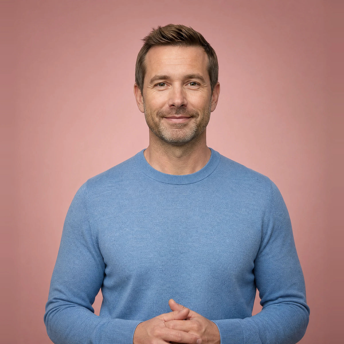 Calm man in a blue sweater with his hands together, smiling