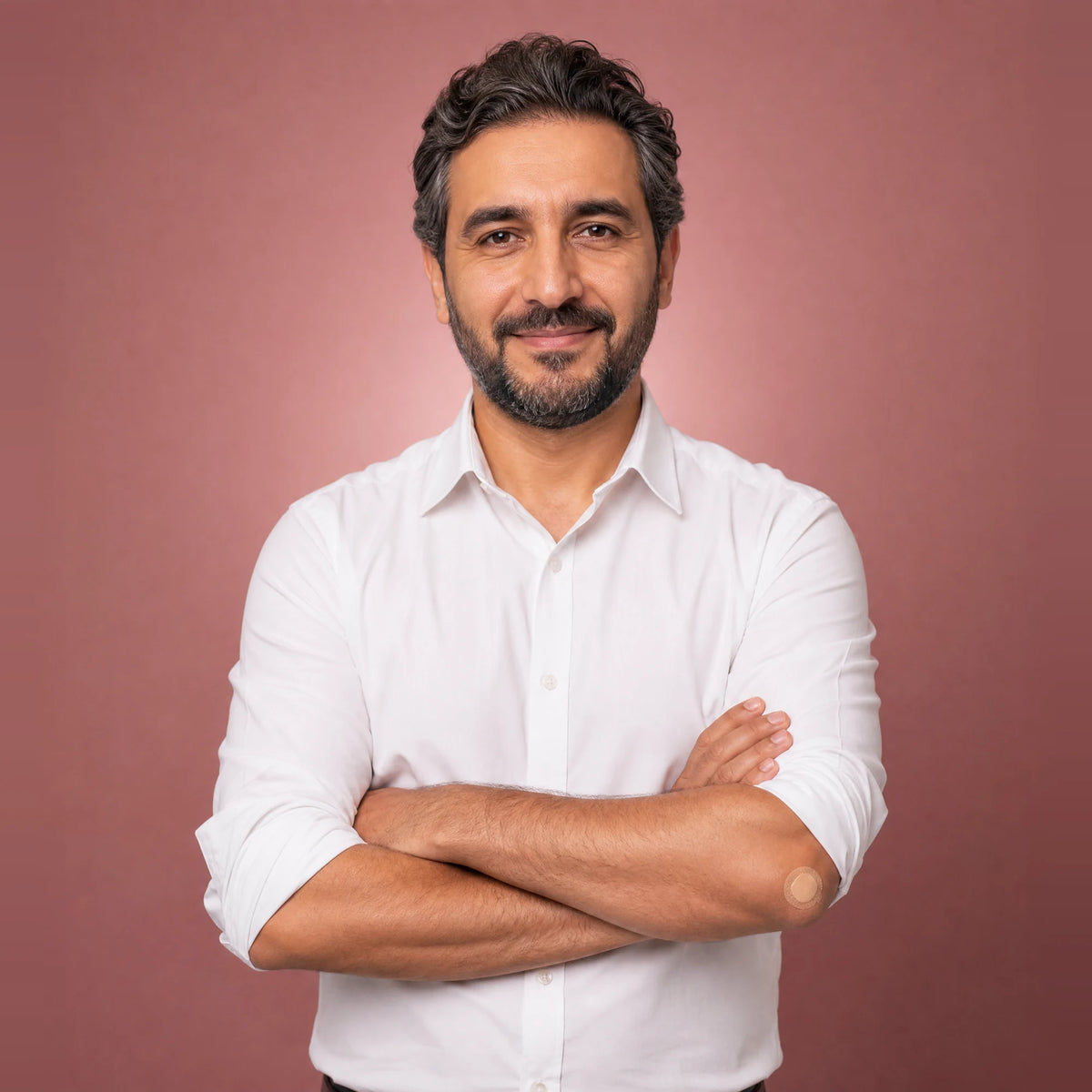Smiling man in a white shirt with his arms crossed, with a small plaster on his arm after a home blood test